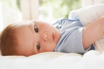 Bébé garçon aux yeux bleus couché sur le dos sur le lit — Photo de stock