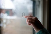 Girl drawing in condensation on window — Stock Photo
