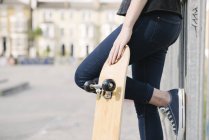 Waist down of female skateboarder leaning against fence in skatepark — Stock Photo