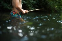 Cropped view of boy waist deep in water holding stick — Stock Photo