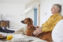 Dog enjoying breakfast in bed with owner — Stock Photo