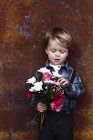 Jovem menino segurando monte de flores — Fotografia de Stock