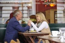 Mature dating couple holding hands at sidewalk cafe table — Stock Photo