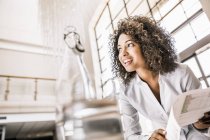 Curly haired business woman with paperwork looking away smiling — Stock Photo
