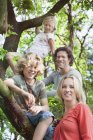 Family in forest climbing tree looking at camera smiling — Stock Photo