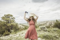 Молода жінка носить червоній сукні і Стетсон танцює на вершині пагорба, коді, Вайомінг, США — стокове фото