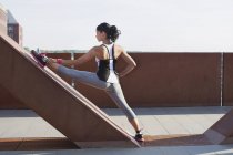 Mulher treinando com perna levantada inclinando-se contra passarela urbana — Fotografia de Stock