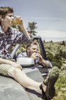 Adolescente sentado en la campana del vehículo todo terreno bebiendo jugo, Bridger, Montana, EE.UU. - foto de stock