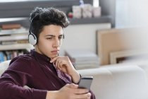 Junger Mann auf Sofa mit Kopfhörer und Smartphone — Stockfoto