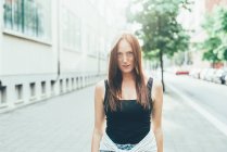 Portrait of freckled young woman with long red hair standing on city street — Stock Photo