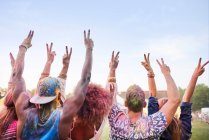 Gruppo di amici al festival, ricoperto di vernice a polvere colorata, braccia alzate, segno di pace con le dita, vista posteriore — Foto stock