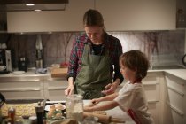 Reife Frau und Sohn rollen Teig auf Küchentheke — Stockfoto