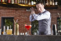 Bartender shaking cocktail shaker in bar — Stock Photo
