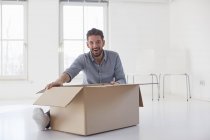 Portrait de jeune homme assis sur le plancher ouvrant boîte en carton dans une nouvelle maison — Photo de stock