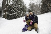 Retrato del hombre adulto medio agachado en la nieve abrazando a su hija - foto de stock