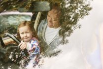 Вид через вітрове скло дочки, що сидить на колінах батька за кермом автомобіля — стокове фото