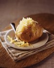 Baked potato with grated cheddar cheese on wooden cutting board — Stock Photo
