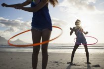 Dos mujeres jóvenes usando hula hoop en la playa - foto de stock