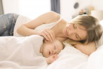 Mãe cuidando do bebê adormecido na cama em casa — Fotografia de Stock