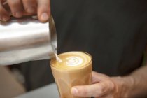 Закрыть руки баристы наливая молоко в кофе в кафе — стоковое фото