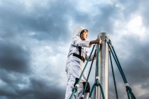 Junge im Astronautenkostüm blickt von oben auf Klettergerüst gegen dramatischen Himmel — Stockfoto