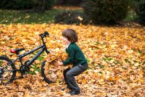 Junge im Park mit Fahrrad spielt im Herbstlaub — Stockfoto