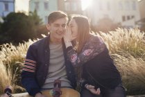 Two friends sitting outdoors, young woman whispering to young man, Bristol, UK — Stock Photo