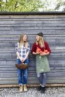 Two friends holding homegrown produce by wooden shed — Stock Photo