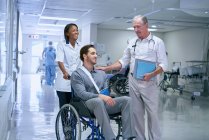 Doctor consulting with man in wheelchair with arm sling — Stock Photo