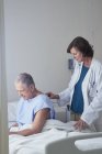 Médico femenino escuchando a un paciente masculino mayor con estetoscopio - foto de stock