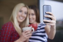 Two female friends, drinking coffee, outdoors, taking self portrait using smartphone — Stock Photo