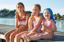 Two sisters and female toddler on pier eating ice cream cones, Lake Seeoner See, Bavaria, Germany — Stock Photo