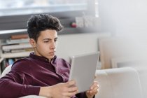 Молодой человек на диване с помощью цифрового планшета — стоковое фото