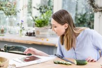 Жінка нарізає огірок цифровим планшетом — стокове фото