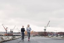 Two female running friends running along dockside — Stock Photo