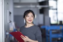 Female worker holding clipboard in factory — Stock Photo