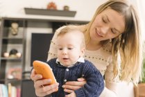 Mother holding baby with toy smartphone at home — Stock Photo