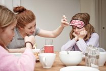Mitte erwachsene Frau am Frühstückstisch, die unter die Schlafmaske der Töchter guckt — Stockfoto