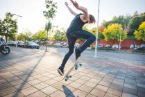 Молодий чоловік міський скейтбордист робить трюк стрибка скейтбордингу на тротуарі — стокове фото