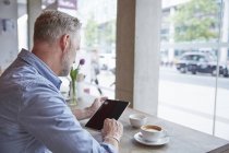 Reifer Mann sitzt im Café, nutzt digitales Tablet, Rückansicht — Stockfoto