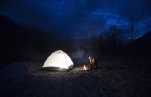 Homem pela fogueira e tenda à noite — Fotografia de Stock