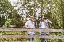Two male adult friends drinking beer at garden fence — Stock Photo