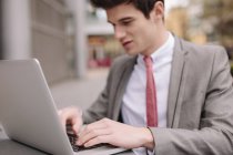 Jovem empresário digitando no laptop no café da calçada — Fotografia de Stock