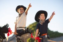Two brothers dressed as cowboys pointing from sand dunes — Stock Photo