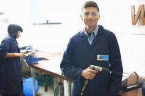 Retrato de estudiante masculino con taladro manual en taller de metalistería universitaria - foto de stock