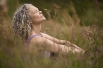Зрелая женщина медитирует в длинной траве — стоковое фото