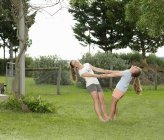 Две сестры держатся за руки и балансируют вместе в саду — стоковое фото