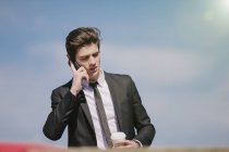 Jungunternehmer spricht mit Smartphone und trinkt Kaffee zum Mitnehmen — Stockfoto