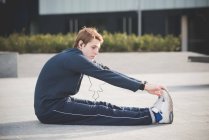 Junger Mann berührt Zehen auf Stadtplatz — Stockfoto