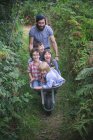 Metà uomo adulto spingendo carriola con ragazzi sorridenti in giardino — Foto stock
